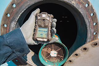 Worker hand holding a gas detector doing a safety inspection for gas at front of a manhole tank.