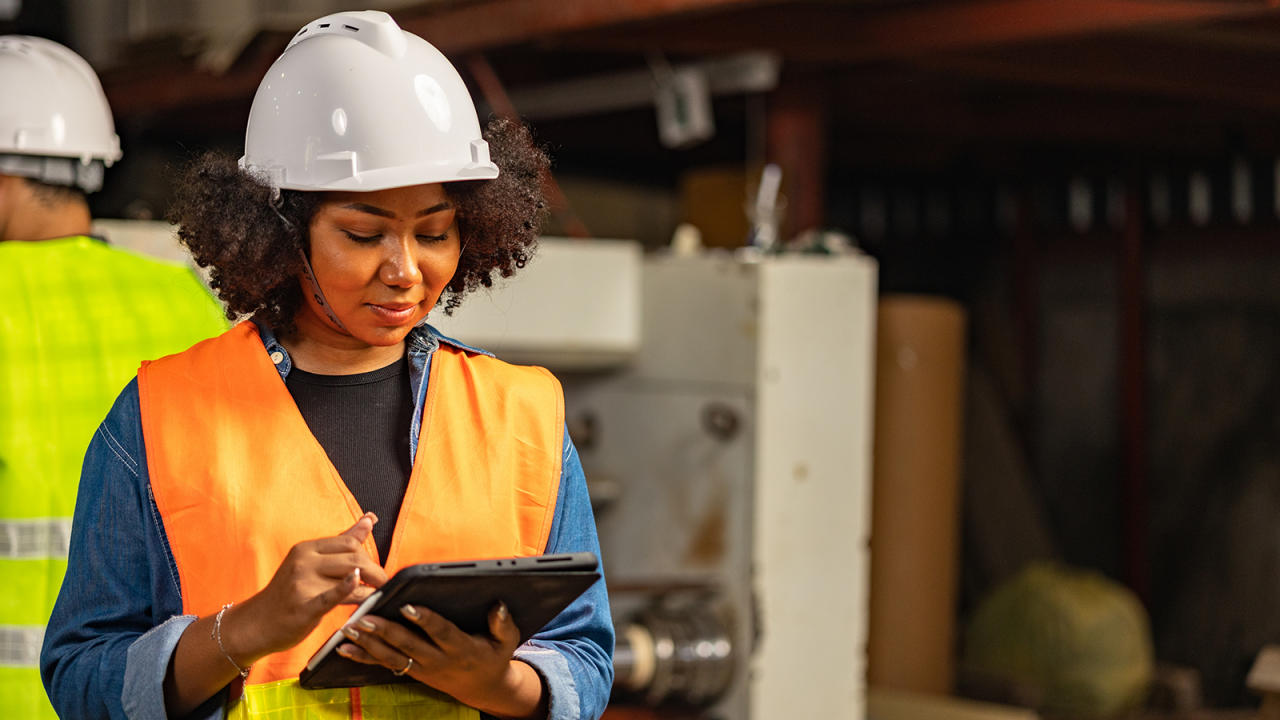 안전 헬멧과 조끼를 착용한 상태에서 태블릿의 MSS를 사용하여 제품의 신뢰성을 분석하고 있는 여성 엔지니어. 